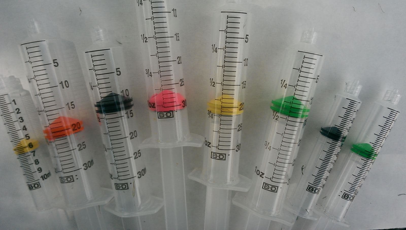 A row of early prototype syringes with black and fluorescent plunger seals.